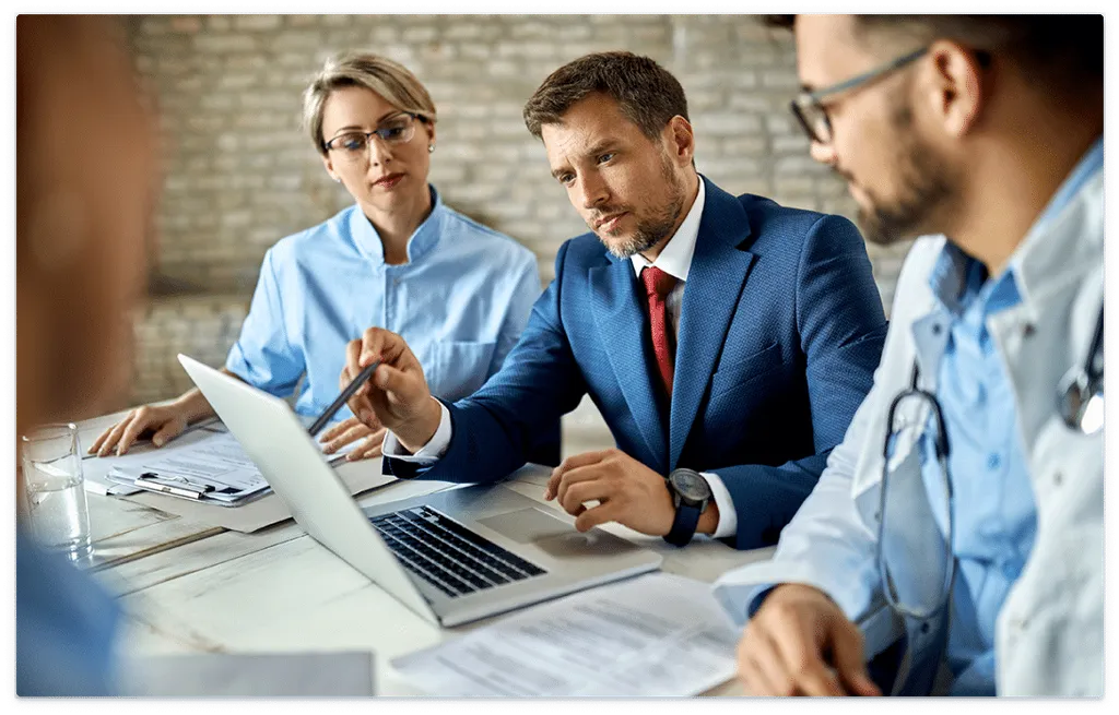 Meeting where business professional gesturing to laptop while a doctor and his colleague look on.