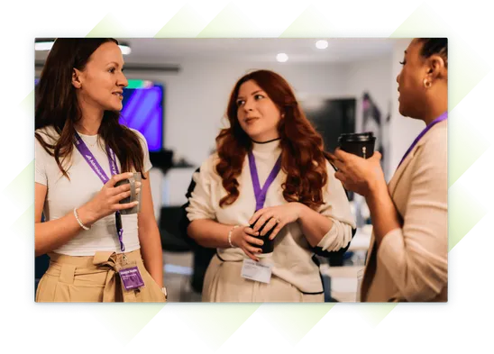 Three female team members at our Customer Summit, chatting and holding coffee cups during a break, wearing Administrate lanyards.