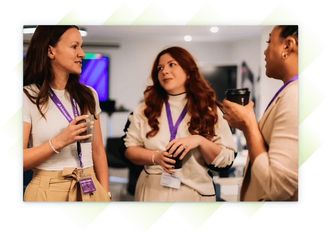 Three female team members at our Customer Summit, chatting and holding coffee cups during a break, wearing Administrate lanyards.