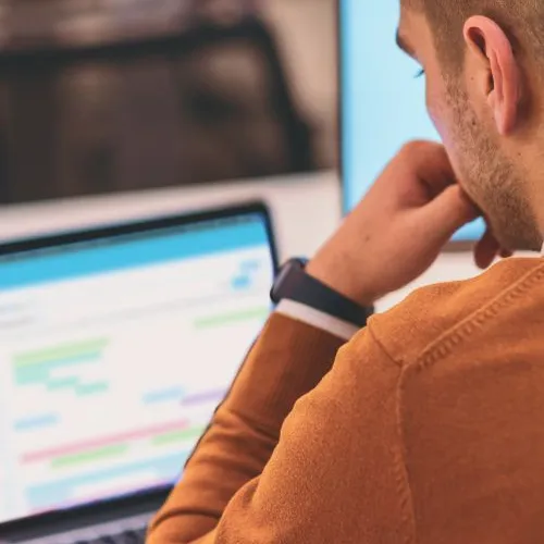 Man looking down at his laptop thoughtfully, with Administrate's AI Scheduler on the screen.