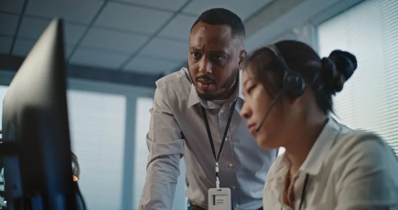 Supervisor at a finance firm looking over the shoulder of one of his colleagues with concern.