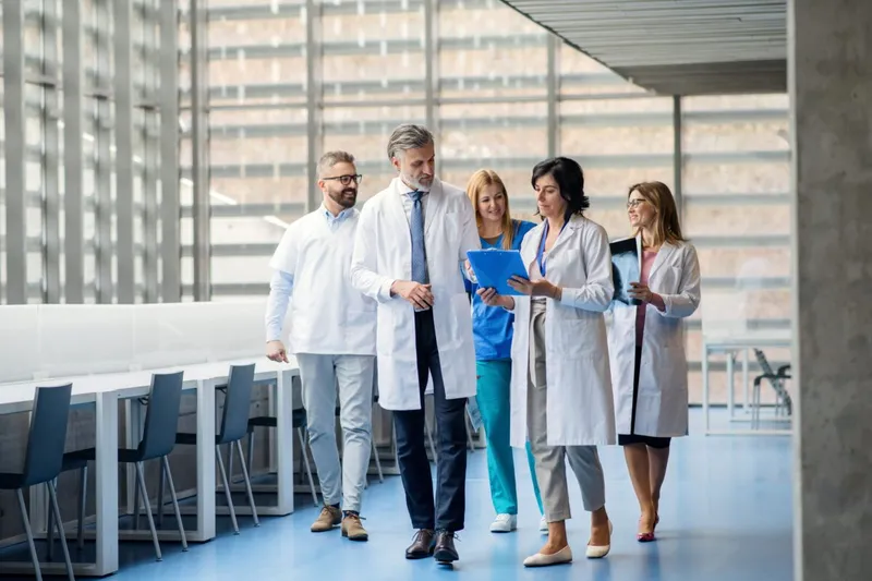 Group of doctors walking together at a building while a medical leader advises his report.