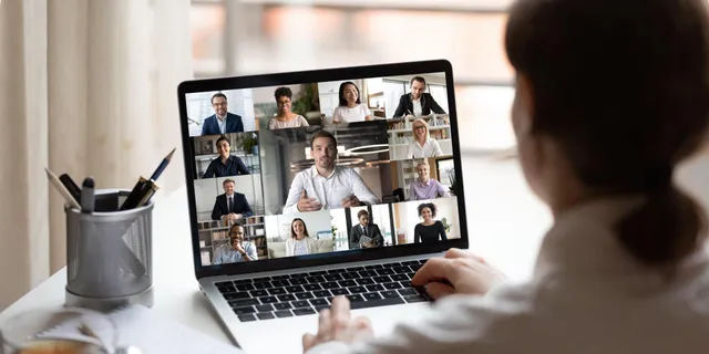 Person viewed from behind participating in a video conference on a laptop, with a grid of 16 colleagues visible on screen.