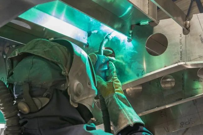 Worker inspecting the interior of a large industrial marine container, with equipment and coiled rope visible inside.