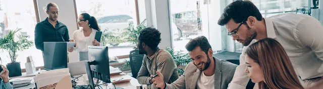 Diverse team of six professionals collaborating in a bright office with floor-to-ceiling windows overlooking a coastal cityscape.
