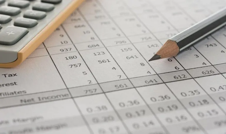 Close-up of a financial spreadsheet with a pencil and calculator, showing rows of numerical data including tax and net income figures.