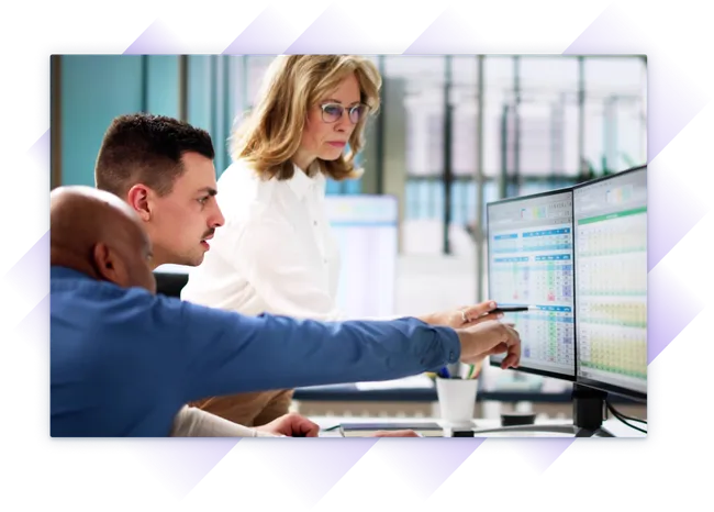 Three professionals review training data on dual monitors in a modern office.