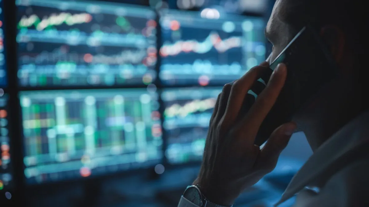 Financial analyst on the phone while looking at stock market dashboards.