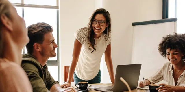 Diverse group of five professionals in a collaborative meeting around a table with laptops and notebooks in a bright modern office.