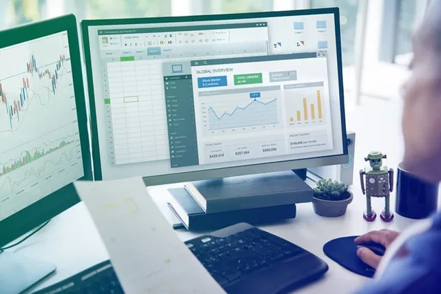 Workspace with a laptop and printed data analytics documents including bar charts, a donut chart, and a revenue report, with an open notebook and pen.