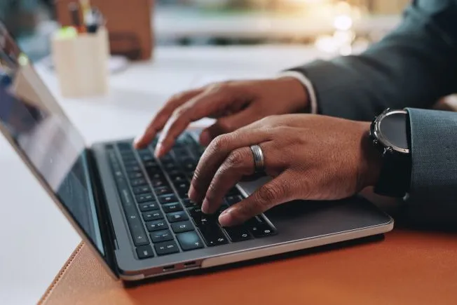 Business person with watch typing on a laptop in his office.