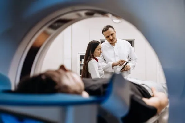 A doctor completes an MRI examination while engaging with a younger doctor.