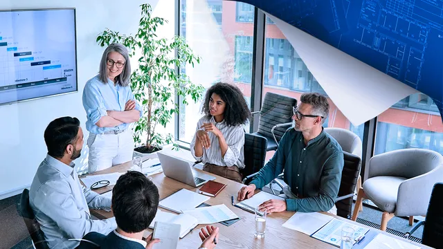 Five professionals in a modern office meeting around a conference table, with city views and data charts displayed on wall monitors.