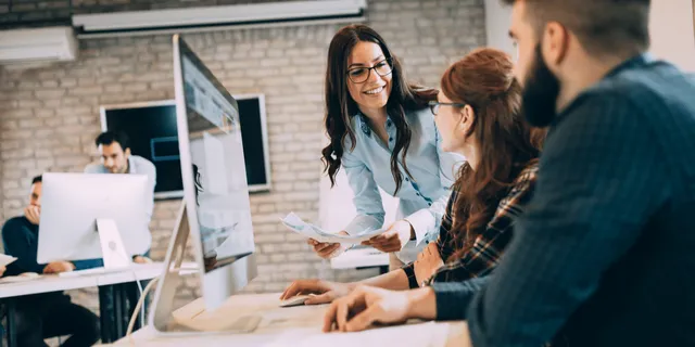 Woman with glasses and a colleague reviewing documents in a collaborative tech office with exposed brick walls and desktop computers.