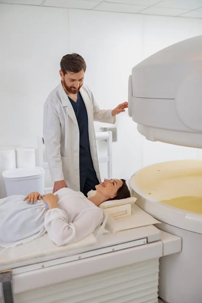 Healthcare professional in a white lab coat operating an MRI machine with a patient on the scanning table in a modern medical facility.