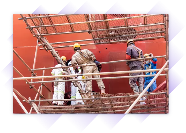 Shipyard crew in safety gear working on scaffolding beside a large vessel.