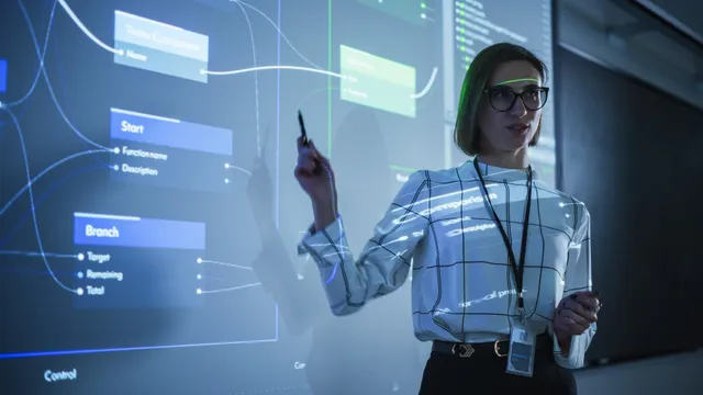 A presenter holding a stylus stands in front of a glass wall projecting a software flowchart and code, surrounded by data visualizations.