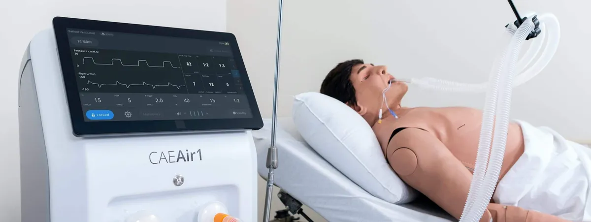 CAE ventilation device next to a medical mannequin on an examination bed in a clinical training environment.