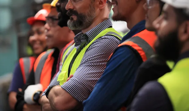 Group of construction workers in high-visibility safety vests and hard hats gathered on a job site.