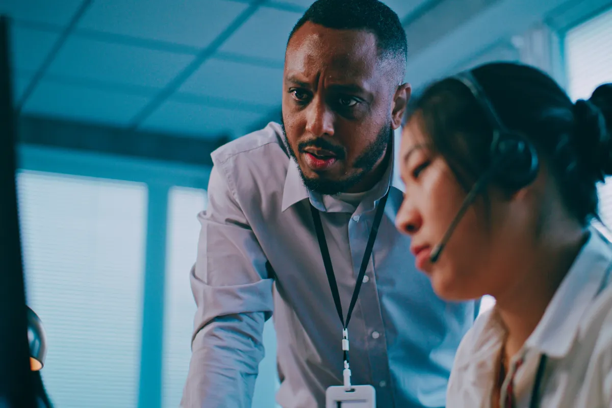 Supervisor at a distributed training firm looking over the shoulder of one of his colleagues with concern.