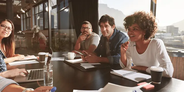 Four professionals seated at a conference table with laptops and notebooks in a modern office with a panoramic mountain view.