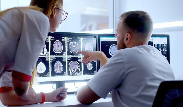 Two medical professionals reviewing brain scan images on dual monitors in a clinical setting.