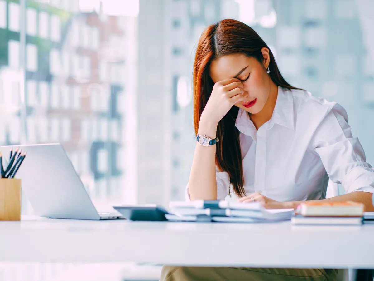 stressed woman at desk holding her nose