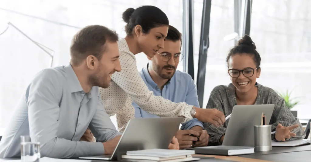 Training team in a boardroom with one member pointing at a laptop that they are all looking at.