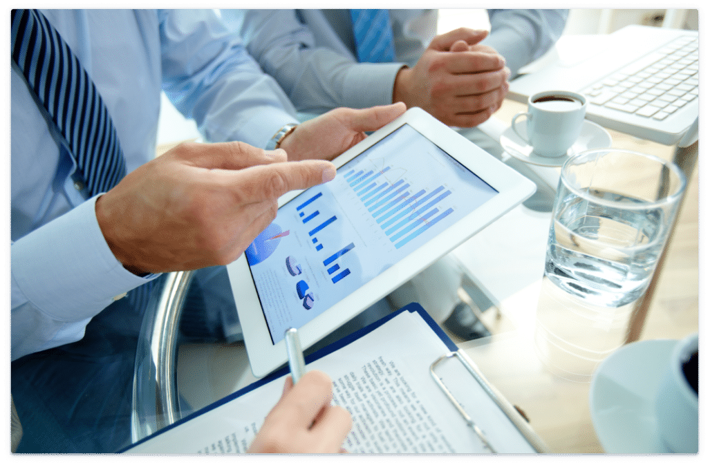 Businessmen in a meeting gesturing at a tablet with charts.