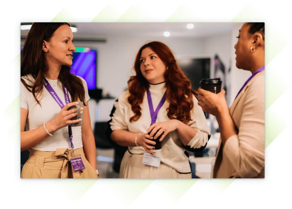 Three female team members at our Customer Summit, chatting and holding coffee cups during a break, wearing Administrate lanyards.